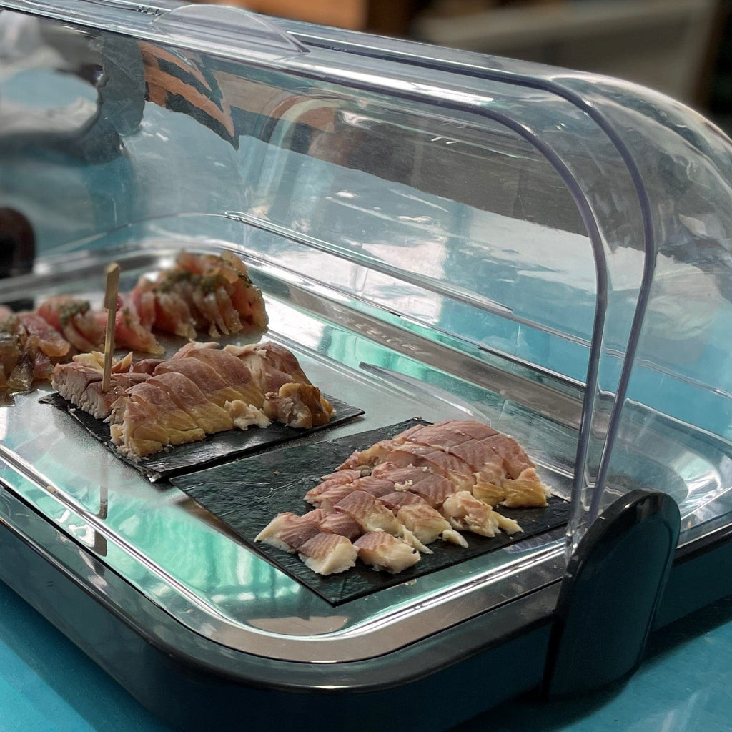 Smoked wiener wels filet sliced on black trays inside clear refrigerated display case.
